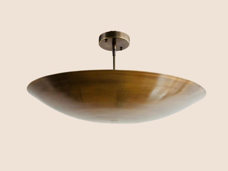 May include: A bronze-colored, bowl-shaped ceiling light fixture. The fixture has a circular base and a central rod connecting to a large, shallow bowl. The light is suspended from the ceiling.