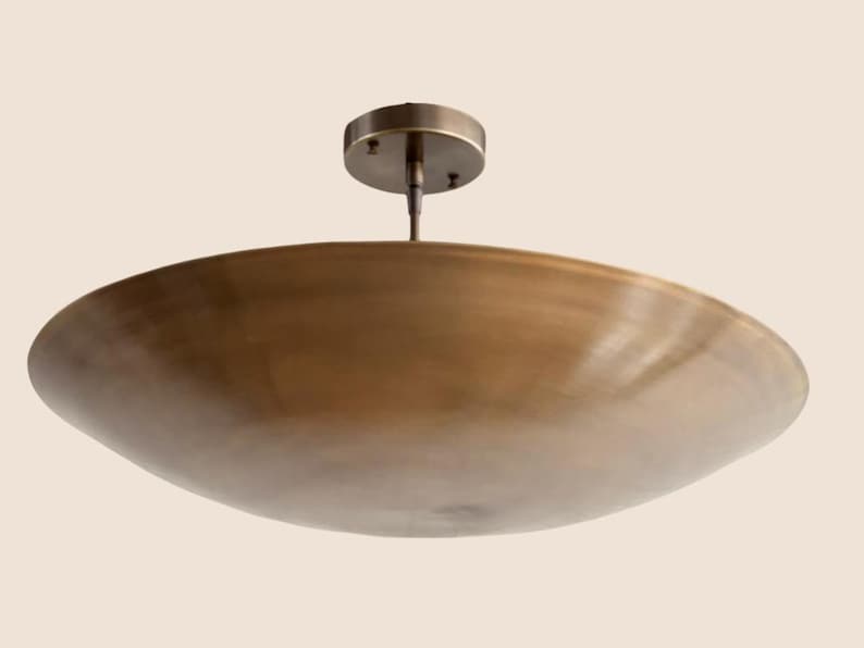 May include: A bronze-colored, shallow, circular ceiling light fixture. The fixture has a wide, bowl-shaped shade and a small, round mounting plate. The light is suspended from a short rod.