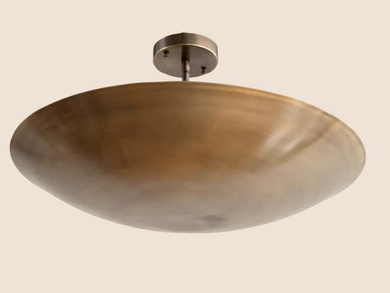 May include: A bronze-colored, bowl-shaped ceiling light fixture. The fixture has a circular base and a stem that connects to the bowl. The bowl has a smooth, curved surface. The light fixture is designed to be mounted on a ceiling.