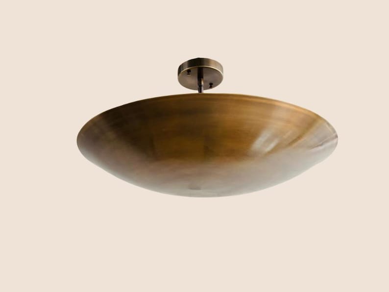 May include: A bronze-colored, shallow bowl-shaped ceiling light fixture. The fixture has a circular mounting plate and a curved, wide shade. The overall design is minimalist and modern, suitable for various interior styles.