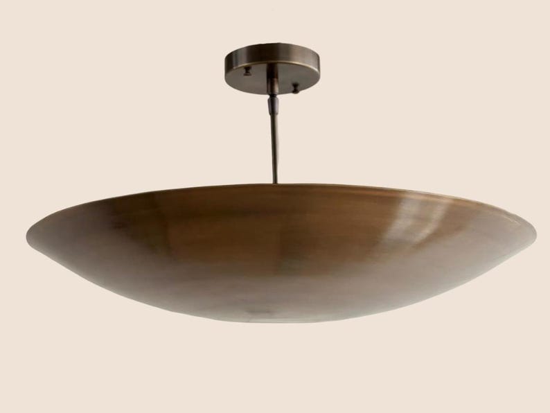 May include: A bronze-colored, bowl-shaped ceiling light fixture. The fixture has a circular base and a slender rod suspending the bowl. The bowl has a wide, shallow design. The light fixture is designed to be mounted on a ceiling.