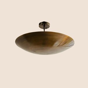 May include: A bronze-colored, shallow, circular ceiling light fixture. The light has a bowl-like shade and a small, round mounting plate. The fixture is suspended from the ceiling by a short rod.