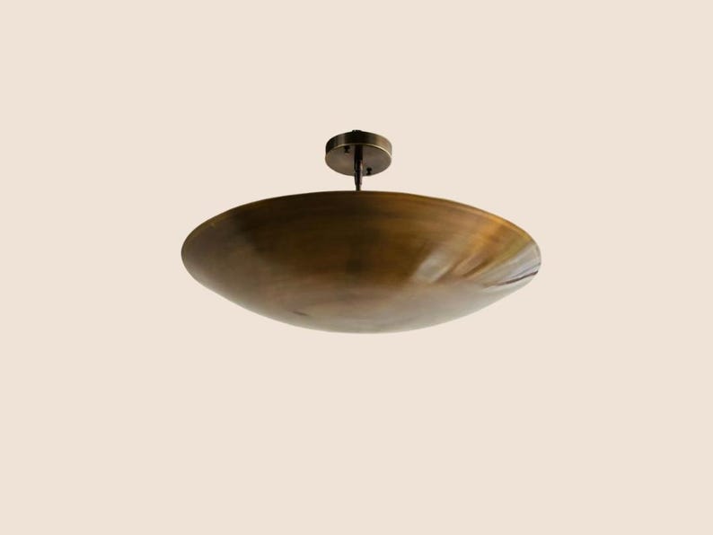 May include: A bronze-colored, shallow, circular ceiling light fixture. The light has a bowl-like shade and a small, round mounting plate. The fixture is suspended from the ceiling by a short rod.
