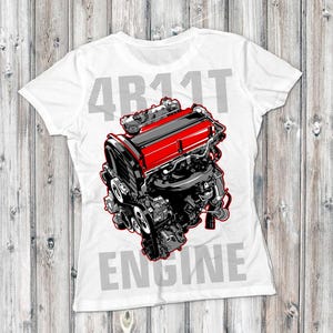 Op de afbeelding: Wit T-shirt met een gedetailleerde illustratie van een rood en zwarte motor. De tekst "4B11T ENGINE" is in grijs boven en onder de motorgrafiek gedrukt. Het T-shirt wordt op een houten achtergrond getoond.