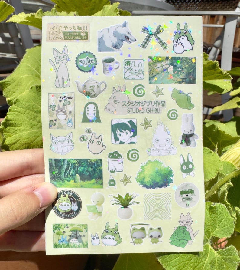 Puede incluir: Una hoja de pegatinas con varios personajes e im&aacute;genes de Studio Ghibli. Las pegatinas incluyen im&aacute;genes de Totoro, un lobo, un gato y otros personajes, con algunos detalles hologr&aacute;ficos. La hoja tiene texto en japon&eacute;s.