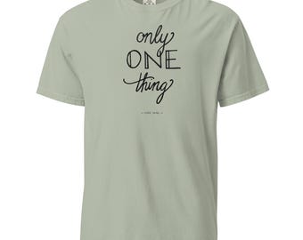 May include: Sage green t-shirt with the words "only ONE thing" in black script. Below the text is "- LUKE 10:42 -" in a smaller font. The shirt has a crew neck and short sleeves.