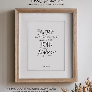 Può includere: Una stampa incorniciata con sfondo bianco e testo nero. Il testo recita "Quando il mio cuore è sopraffatto, conduci me alla roccia che è più alta di me" e "Salmo 61:2".