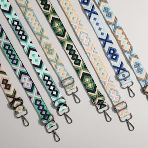 May include: A collection of colorful, patterned bag straps. Each strap features a unique geometric design in various colors, including green, blue, purple, and beige. The straps have metal hardware for attachment.