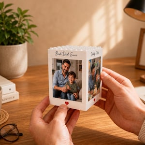 May include: A white, square, block-style photo frame with a textured top surface resembling building bricks. The frame features two visible sides, each displaying a printed photograph of a man and a child, with the text Best Dad Ever and Daddy & Me.