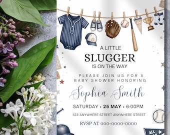 Peut inclure: Une carte d'invitation pour baby shower sur le thème du baseball avec un body à rayures bleu marine, une casquette, un gant, une balle, une batte et un trophée suspendus à une corde. Le texte indique A LITTLE SLUGGER IS ON THE WAY pour Sophia Smith.