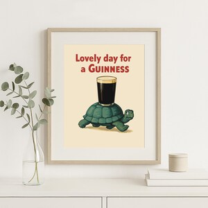 Puede incluir: Impresi&oacute;n enmarcada con una ilustraci&oacute;n de una tortuga verde con un vaso de Guinness. El texto "Lovely day for a Guinness" es rojo. La obra de arte tiene un estilo vintage, ideal para un bar.