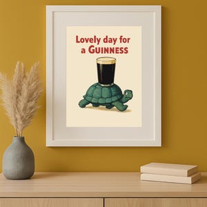 Puede incluir: Impresi&oacute;n enmarcada que presenta una tortuga de dibujos animados que lleva una pinta de Guinness. El texto "Lovely day for a Guinness" es rojo. La obra de arte se muestra en un marco blanco.