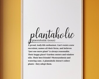 Puede incluir: Un cartel enmarcado con la palabra "plantaholic" en escritura elegante. La definición de abajo describe a un entusiasta de las plantas. El marco es de color claro y el fondo es blanco. El cartel se muestra contra una pared amarilla.