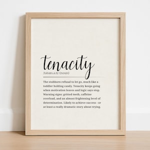 May include: A framed print featuring the word "tenacity" in cursive script. The definition below describes tenacity as the stubborn refusal to let go, with warning signs like gritted teeth and caffeine overload. The print is in a light wood frame.