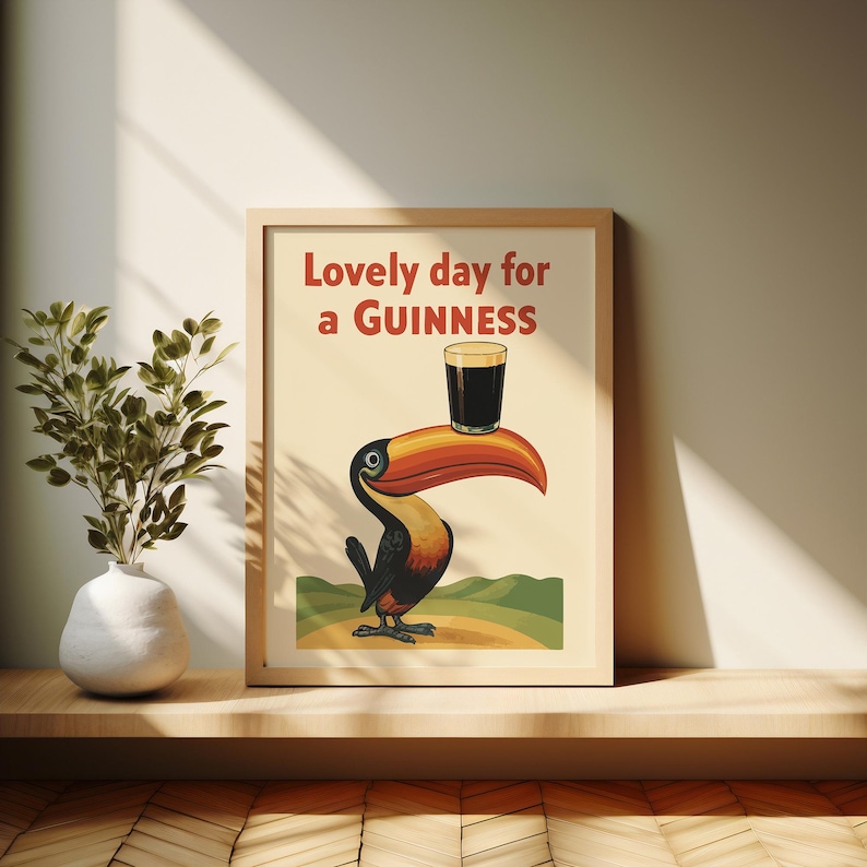 May include: Framed print featuring a cartoon toucan with a large orange beak, holding a pint of Guinness. The text "Lovely day for a Guinness" is displayed in red. The artwork is set against a beige background.