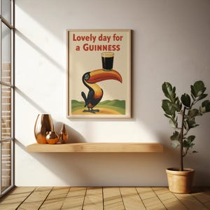 May include: A framed vintage-style poster featuring a toucan holding a pint of Guinness on its beak. The poster has the text "Lovely day for a Guinness" in red. The toucan is black, orange, and yellow, set against a cream background.