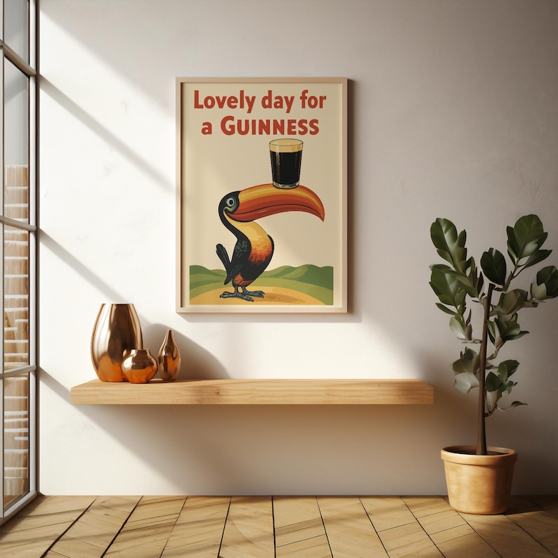 May include: A framed vintage-style poster featuring a toucan holding a pint of Guinness on its beak. The poster has the text "Lovely day for a Guinness" in red. The toucan is black, orange, and yellow, set against a cream background.