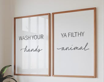 May include: Two framed art prints with wooden frames. The left print reads "WASH YOUR hands" in black script. The right print says "YA FILTHY animal" in black script. The prints are on a white background.