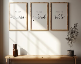 May include: Three framed prints with white backgrounds and black text. The text on the prints reads "The best memories are made gathered around the table". The prints are hanging on a white wall with a wooden bench in front of them.