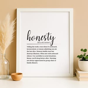 May include: A framed print with the word "honesty" in a stylish script font. The definition of honesty is provided below the word, describing it as telling the truth, even when it's awkward. The print is in a white frame.