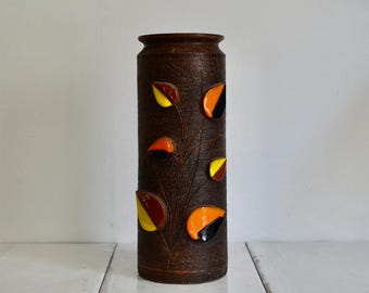 May include: A brown ceramic vase with a textured surface and colorful geometric leaf designs in shades of orange, yellow, and black.
