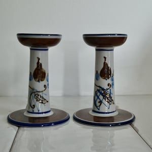 Puede incluir: Un par de candelabros de cer&aacute;mica con un dise&ntilde;o floral marr&oacute;n, blanco y azul. Los candelabros tienen forma de pedestal con una base ancha y una parte superior estrecha.