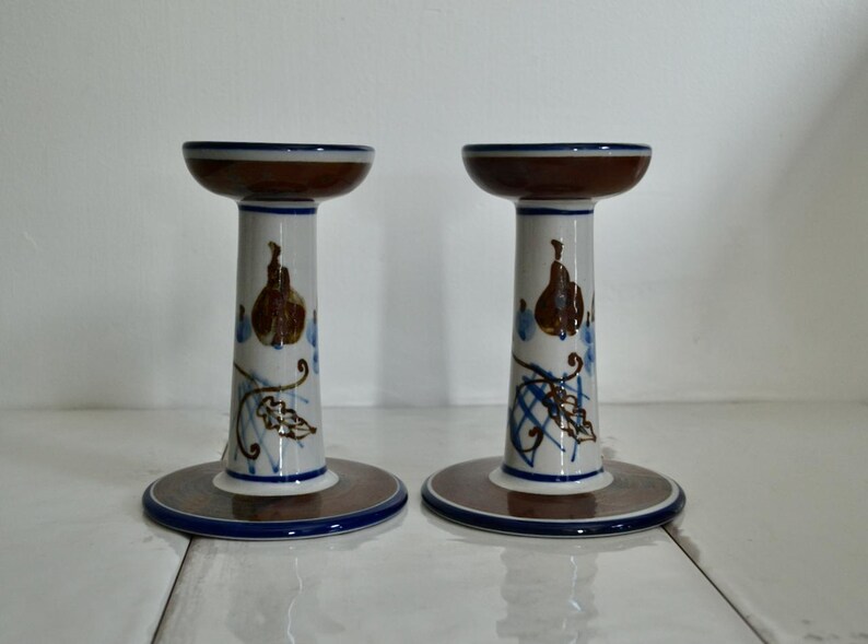 Puede incluir: Un par de candelabros de cer&aacute;mica con un dise&ntilde;o floral marr&oacute;n, blanco y azul. Los candelabros tienen forma de pedestal con una base ancha y una parte superior estrecha.