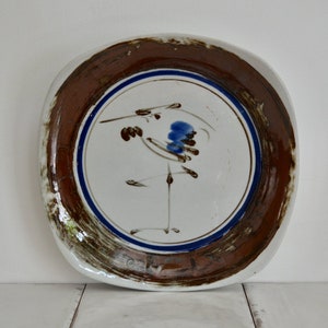 May include: A white ceramic plate with a brown rim and a blue and brown stylized bird design.