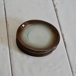 May include: A stack of four brown and white ceramic plates with a glazed finish.
