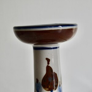 Puede incluir: Un portavelas de cer&aacute;mica blanca con la parte superior marr&oacute;n y un borde azul. El portavelas presenta un dise&ntilde;o floral en marr&oacute;n y azul.