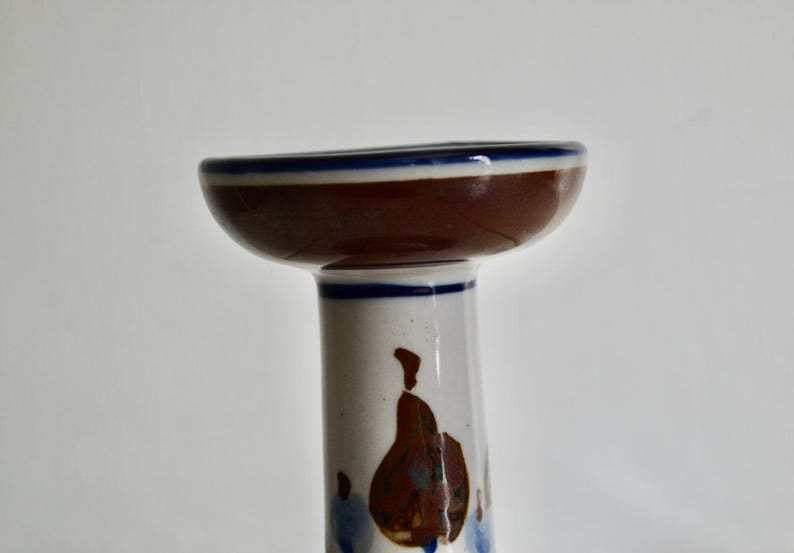 Puede incluir: Un portavelas de cer&aacute;mica blanca con la parte superior marr&oacute;n y un borde azul. El portavelas presenta un dise&ntilde;o floral en marr&oacute;n y azul.