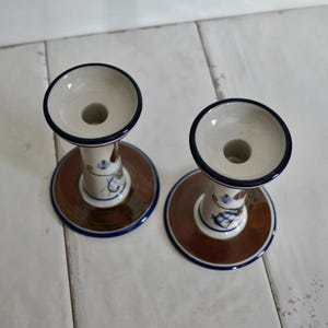 Puede incluir: Dos candelabros de cer&aacute;mica con un dise&ntilde;o floral marr&oacute;n, azul y blanco. Los candelabros tienen una base ancha y una parte superior estrecha con un agujero para una vela.