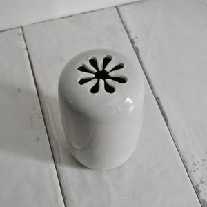 May include: White ceramic vase with a flower-shaped opening at the top.