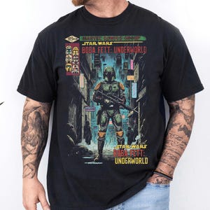 May include: Black t-shirt featuring a Star Wars comic book graphic. The graphic depicts Boba Fett in a futuristic city setting, with the text "STAR WARS BOBA FETT: UNDERWORLD" displayed prominently. The shirt is made of a soft material.