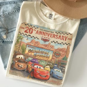 Puede incluir: Una camiseta de color crema con un estampado gr&aacute;fico que celebra el 20 aniversario de la pel&iacute;cula Cars. El dise&ntilde;o incluye personajes como Rayo McQueen y Mate frente al letrero de Radiator Springs con el texto 2006-2026.