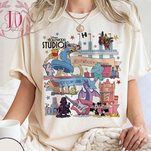 Può includere: Una maglietta bianca con una grafica colorata della mappa del parco Disney Hollywood Studios. La grafica include le parole "Disney Hollywood Studios" e "Toy Story Land".