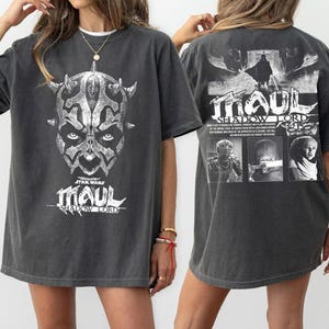 Könnte beinhalten: Dunkelgraues T-Shirt mit einer Grafik von Darth Maul aus Star Wars. Die Vorderseite zeigt ein detailliertes Gesichts-Bild mit dem Text "MAUL" und "STAR WARS". Die Rückseite hat eine größere Grafik mit dem Text "MAUL SHADOW LORD".