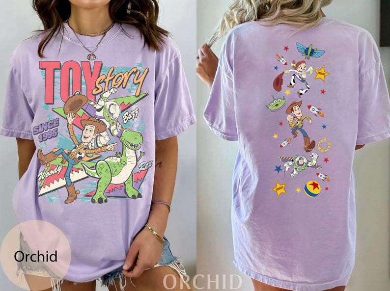 May include: A lilac t-shirt with a Toy Story design. The front has the Toy Story logo and characters Woody, Buzz, and Rex. The back features various characters and elements from the film, including rockets and stars. The text reads "TOY STORY" and "SINCE 1995".