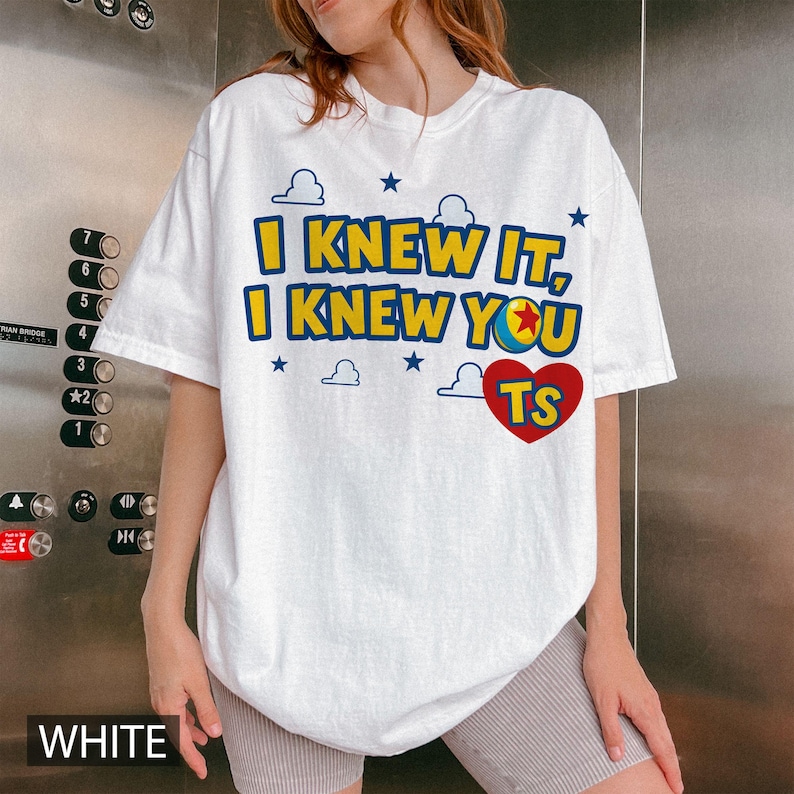 May include: A white short-sleeve t-shirt featuring the blue and yellow text I KNEW IT, I KNEW YOU, a colourful ball icon, a red heart with the letters TS, and small blue cloud and star graphics printed on the front of the garment.