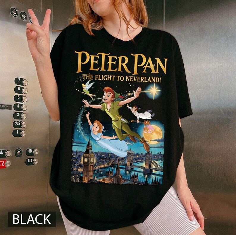 May include: Black t-shirt with a gold print of Peter Pan and friends flying over London, with the text "PETER PAN THE FLIGHT TO NEVERLAND!". The word "BLACK" is printed at the bottom of the shirt.