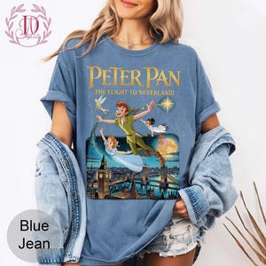 May include: A blue t-shirt with a Peter Pan graphic. The design shows Peter Pan, Wendy, Tinkerbell, and John flying over London. The text on the shirt reads "Peter Pan: The Flight to Neverland!"