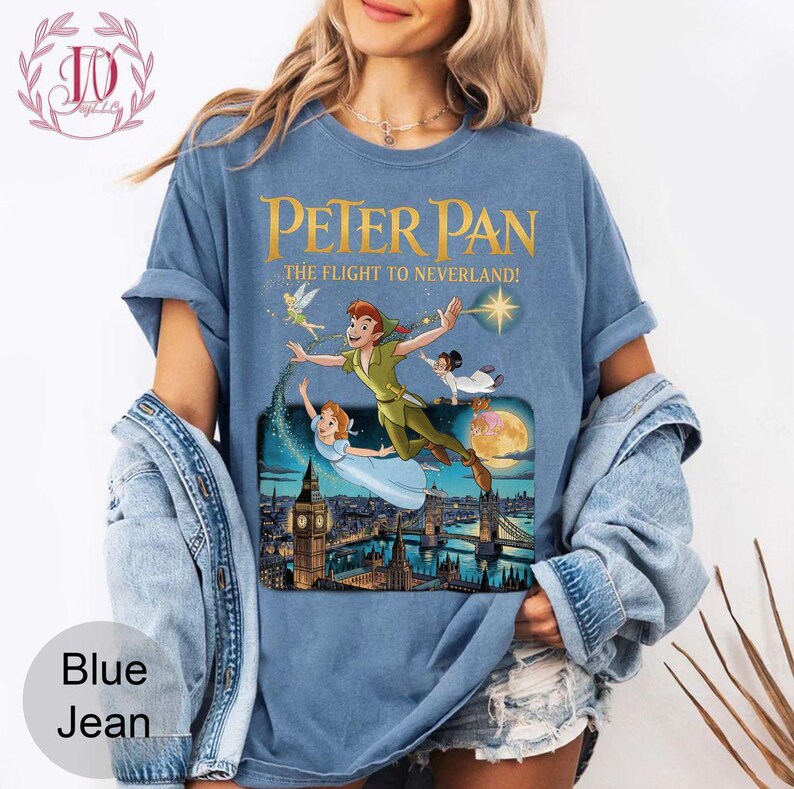 May include: A blue t-shirt with a Peter Pan graphic. The design shows Peter Pan, Wendy, Tinkerbell, and John flying over London. The text on the shirt reads "Peter Pan: The Flight to Neverland!"