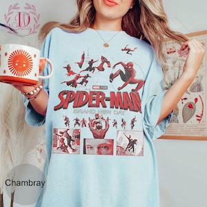 May include: Light blue t-shirt featuring the Spider-Man logo and graphics from the Marvel Studios film "Spider-Man: Brand New Day." The design includes illustrations of Spider-Man in action poses. The shirt is a chambray color.