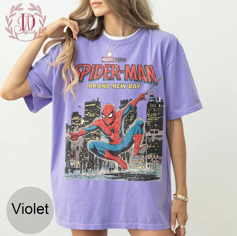 Puede incluir: Camiseta violeta con un gr&aacute;fico de Spider-Man de Marvel Studios. El dise&ntilde;o incluye el texto "SPIDER-MAN BRAND NEW DAY" y una ilustraci&oacute;n de Spider-Man contra un horizonte urbano. La camiseta tiene mangas cortas y cuello redondo.