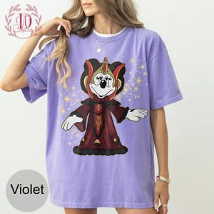 Puede incluir: Camiseta de color violeta con un personaje de dibujos animados con un atuendo rojo y dorado. El gr&aacute;fico incluye un personaje con cara blanca, ojos negros y un tocado rojo y dorado. La camiseta tiene un corte holgado y mangas cortas.