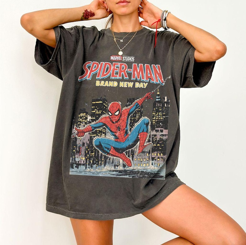 Puede incluir: Camiseta gris oscuro con un gr&aacute;fico de Spider-Man de Marvel Studios. El dise&ntilde;o incluye las palabras "Spider-Man Brand New Day" y una ilustraci&oacute;n de Spider-Man en acci&oacute;n contra un horizonte urbano.