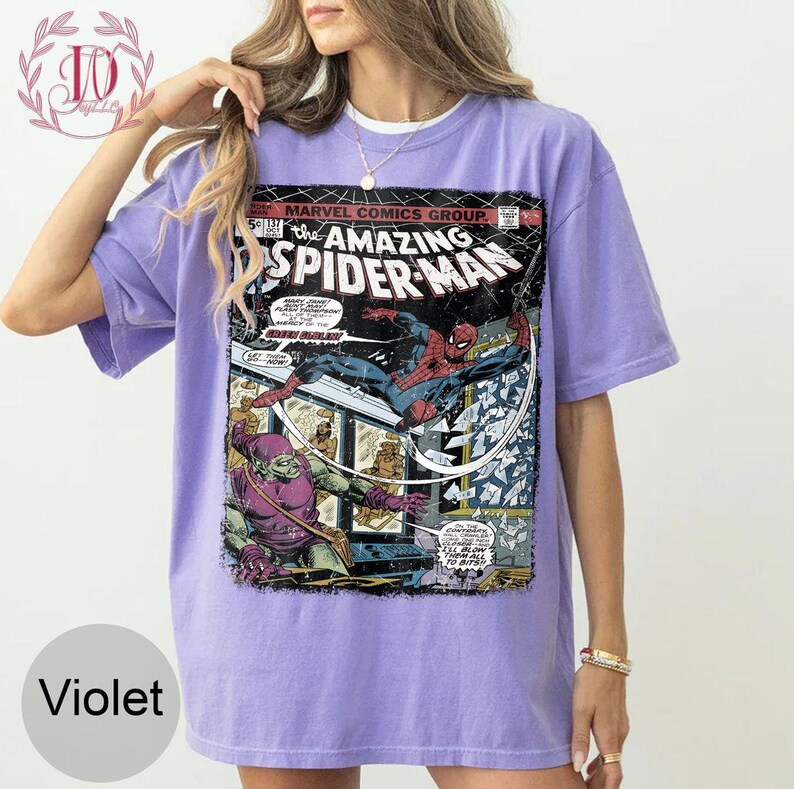 May include: Violet-colored t-shirt featuring a comic book cover of "The Amazing Spider-Man." The graphic includes Spider-Man in action, along with the Green Goblin. The shirt has short sleeves and a crew neck.