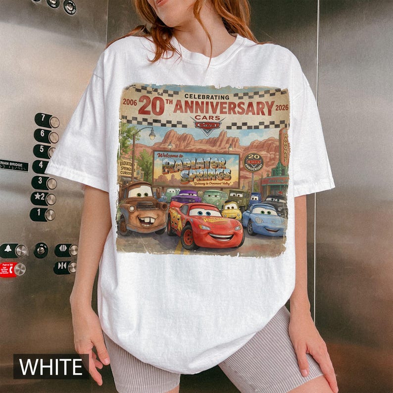 Puede incluir: Una camiseta blanca con un estampado gr&aacute;fico que celebra el 20&ordm; aniversario de la pel&iacute;cula Cars. El dise&ntilde;o muestra personajes de Radiator Springs, incluidos Rayo McQueen y Mate, sobre un fondo de paisaje des&eacute;rtico.