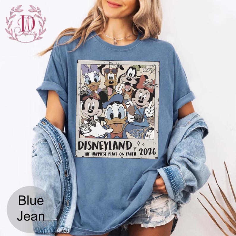 K&ouml;nnte beinhalten: Blaues Jeans-T-Shirt mit einem Retro-Grafikdesign von Disney-Figuren, darunter Micky Maus und Donald Duck. Der Aufdruck lautet "Disneyland, The Happiest Place on Earth 2026."