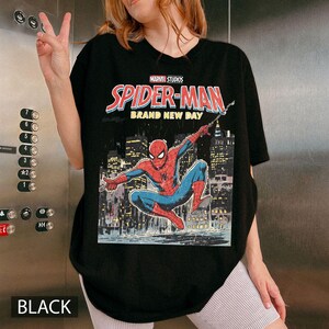 Puede incluir: Camiseta negra de Spider-Man con un gr&aacute;fico de c&oacute;mic. El gr&aacute;fico incluye el texto "MARVEL STUDIOS SPIDER-MAN BRAND NEW DAY" y una ilustraci&oacute;n de Spider-Man. La palabra "BLACK" est&aacute; en la parte inferior.
